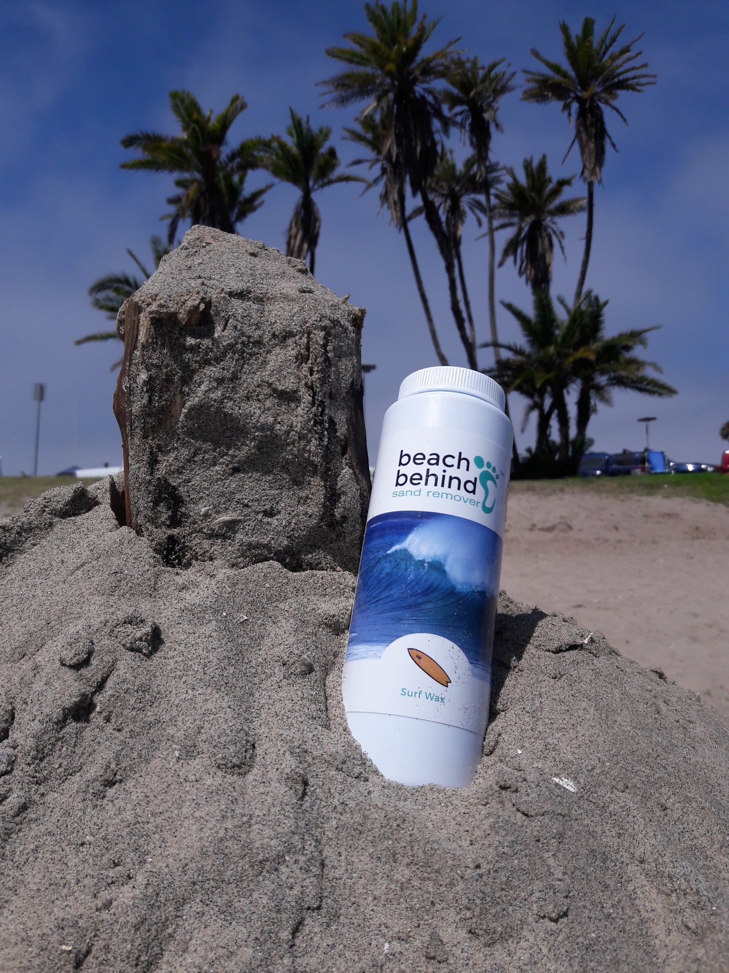 bottle of sand remover sitting on a sand castle next to palm trees in San Diego