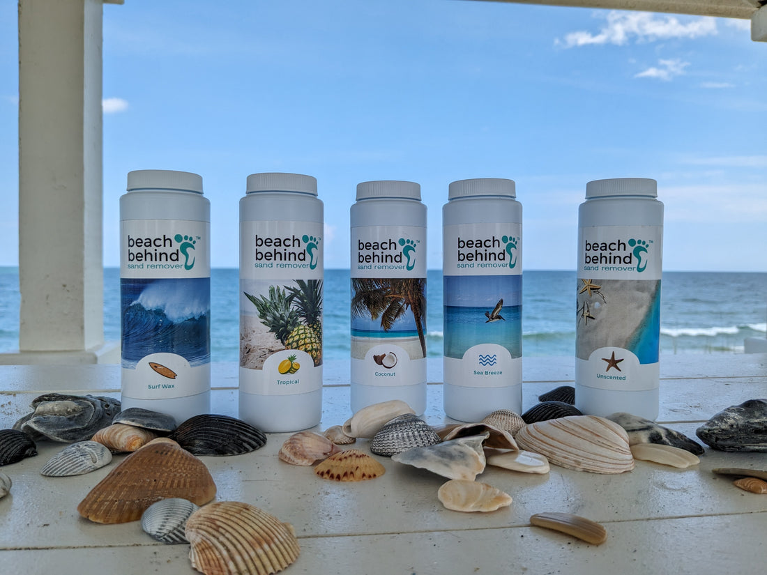 bottles of beach sand remover on a table filled with sea shells with a beach scene behind